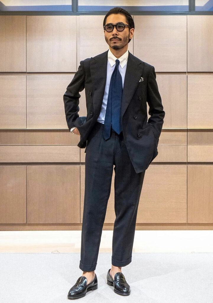 Black suit and a blue white-collar shirt, navy tie, and black loafers