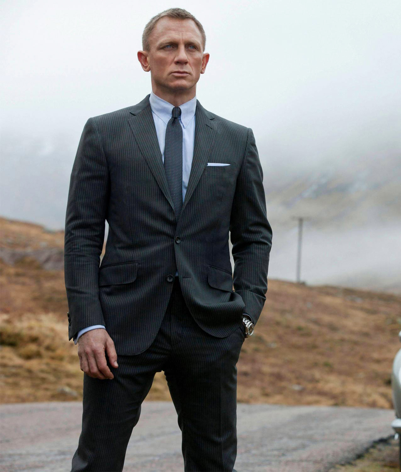 James Bond wears charcoal grey suit with white dress shirt and dark grey tie