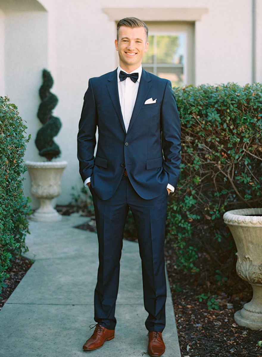 Navy suit with white dress shirt, black bow tie, and brown derby shoes