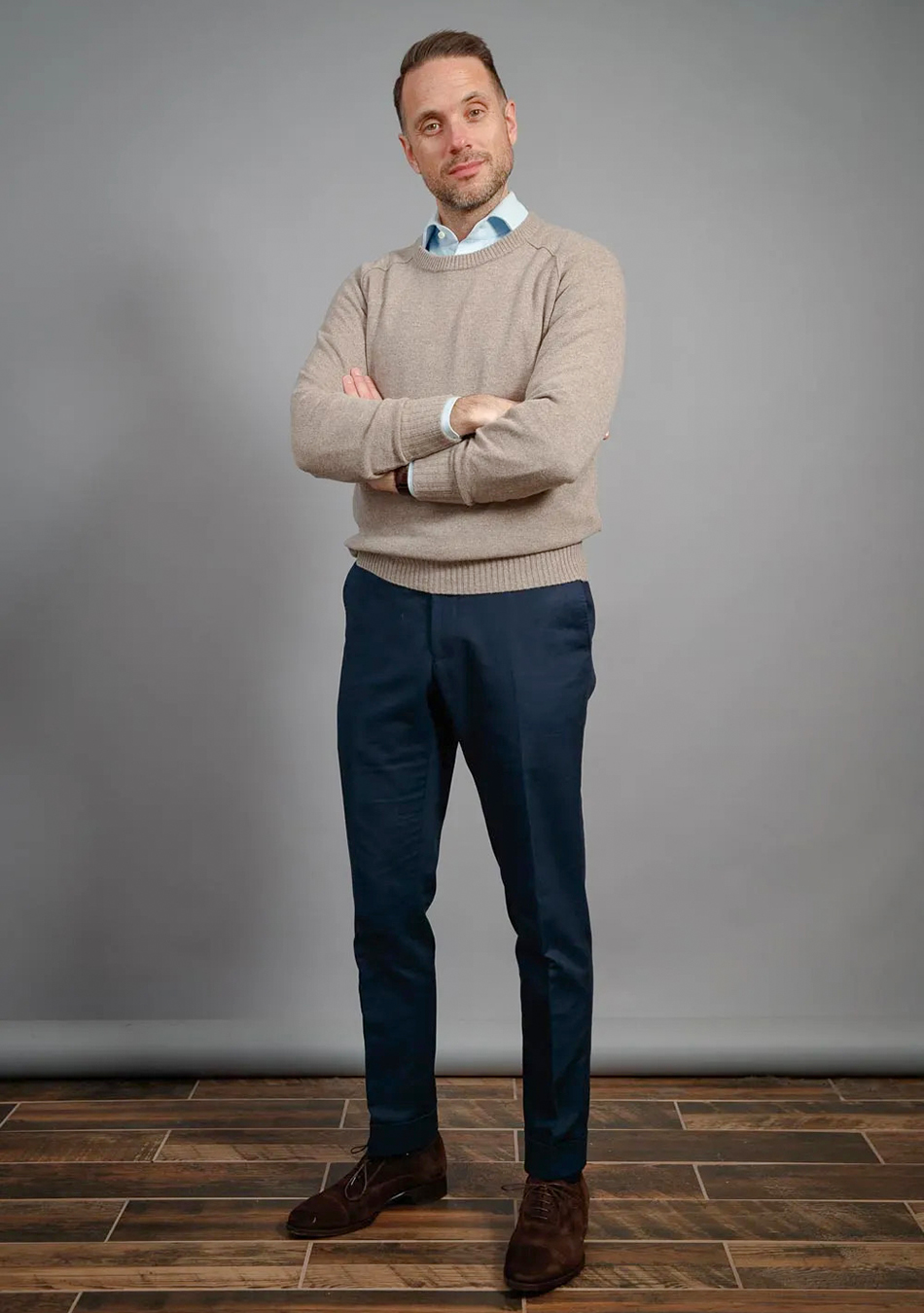 Tan crew neck sweater, navy pants, light blue shirt, and brown suede oxfords