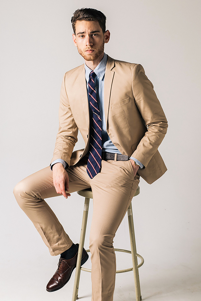 Wearing a tan suit with a light-blue dress shirt, navy striped tie, and brown Oxford shoes