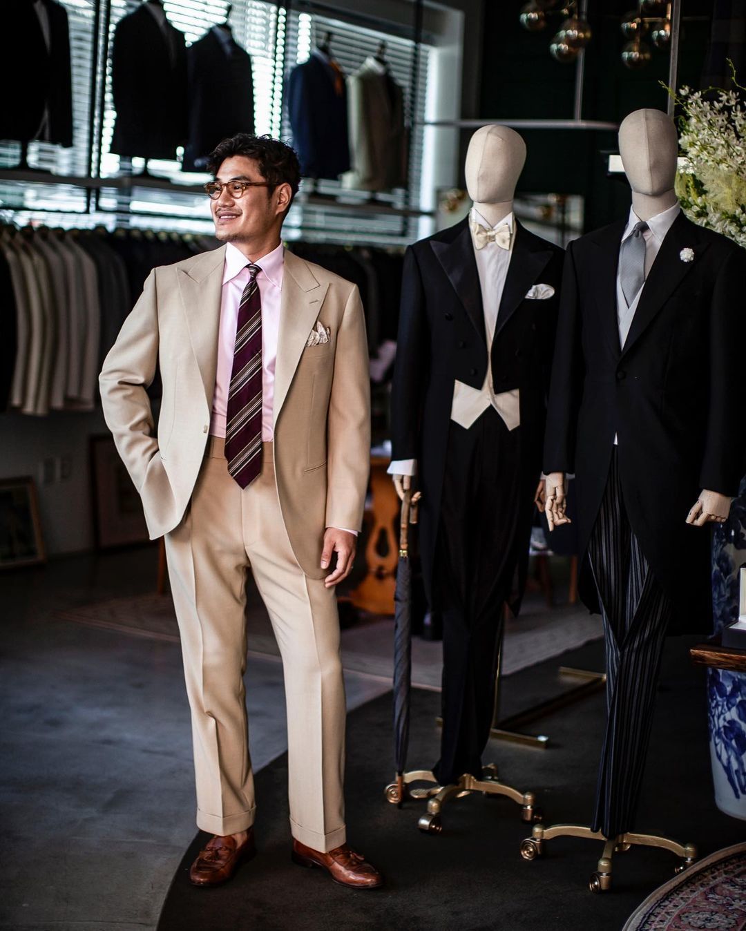 Wearing a tan suit with a light pink shirt, red striped tie, and brown loafers